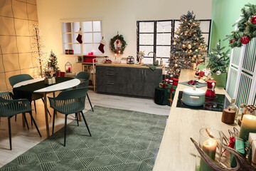 Interior of stylish kitchen with green counters, Christmas tree and dining table