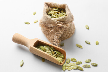 Bag and scoop with pumpkin seeds on light background