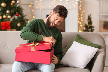 Happy man opening Christmas gift at home