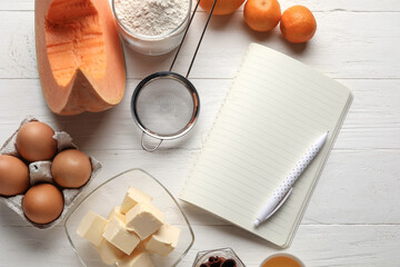 Recipe book and ingredients for pumpkin pie on white wooden background