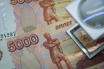 Verification of Russian banknotes for authenticity under a magnifying glass. Used money. Selective...