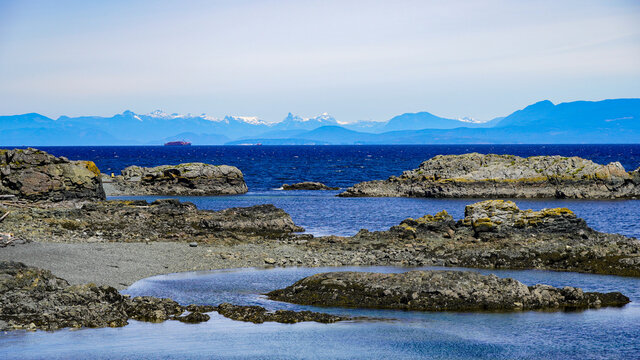 Beautiful sea view with snow mountains at far and rugged rocks near the coast against blue sky and sea water in Neck Point Nanaimo
