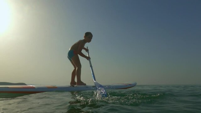 Little child boy have fun surfing on sup or standup paddle board over sea water surface. Low-angle pov