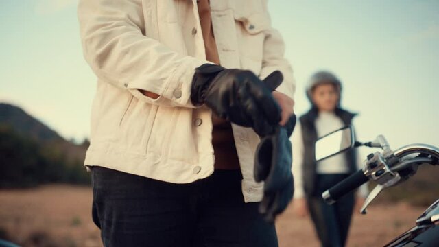 Man Wears Black Leather Gloves With Blurred Image Of Woman In Background Before Riding Motorcycle. - crop shot
