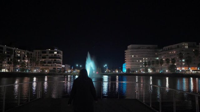 A girl is walking to the fountain at night in Port Marianne