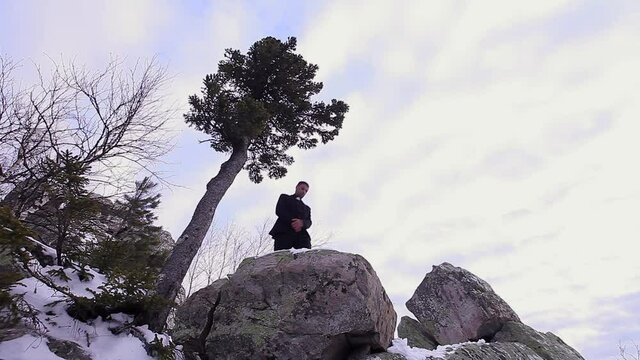 the priest preaches on the mountain. A man in the clothes of a pastor stands on a stone. Winter and cold in the mountains