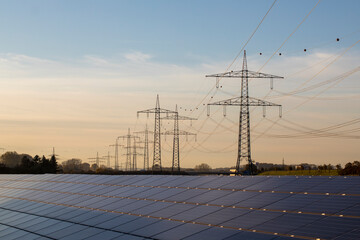 Renewable energy, large field of solar panels, solar panels and high voltage electricity pylons at...