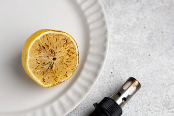 half grilled lemon on the ceramic plate and gas burner on the grey background