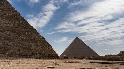 Fototapeta na wymiar Two great pyramids of Giza - Cheops and Chephren on the background of blue sky and clouds. The masonry on the walls is visible. At the foot there are horses harnessed to carts. Egypt