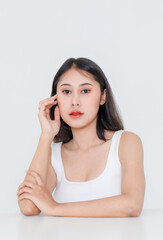 Facial beauty shot of  Asian short black hair model with makeup red lipstick in tank top vest undershirt sitting at table posing crossed arm look at camera on white background