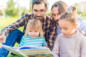 gay male couple with their children reading a book.