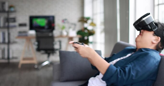 Side view of cheerful mature woman in VR headset playing challenging videogame while sitting on sofa on weekend day