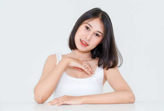 Portrait beauty shot, close up of millennial Asian short black hair model with makeup red lip in tank top undershirt sitting at table posing look at camera on white background