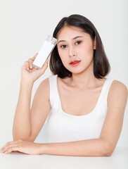 Portrait beauty shot of millennial young Asian short black hair female model in tank top vest undershirt holding natural serum facial cream skincare bottle package in hand on white background