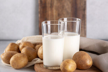 Vegan plant based milk in two transparent glasses. Alternative potato milk and potato tubers on gray table