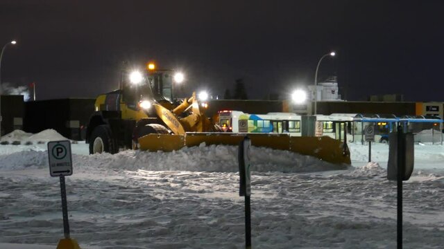 Industrial snow plower clearing snow from city streets at night after snow storm