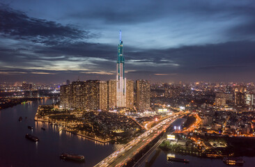 Drone view of busy highway crossing bridge and river to large illuminated city and high rise tower at night. Spectacular and dramatic featuring boat and motor vehicle traffic.