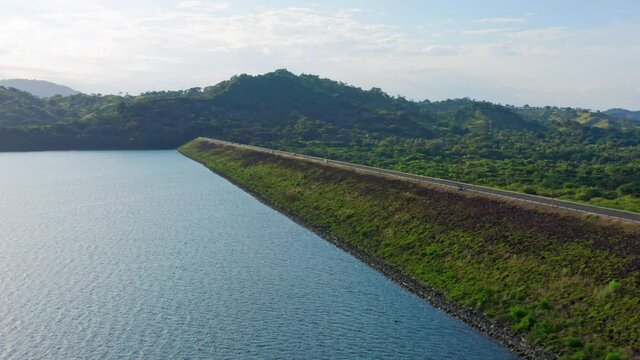 Cars driving on road over Hatillo dam edge, Dominican Republic. Aerial forward