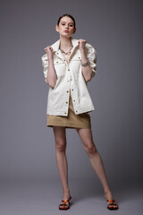 High fashion photo of a beautiful elegant young woman in a pretty white shirt, beige sand skirt,  accessories  posing on gray background. Studio Shot. Slim figure.