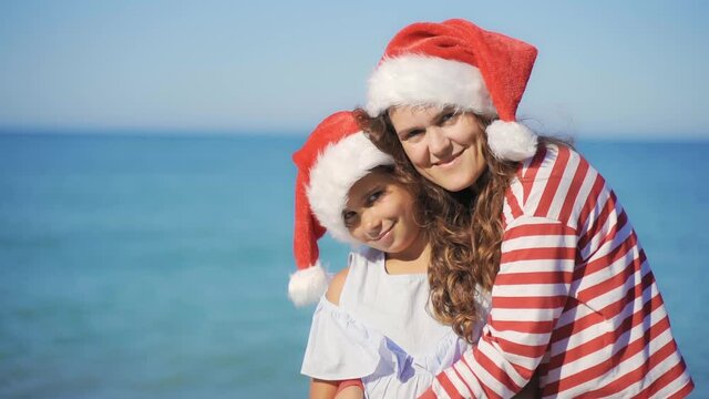 Happy Mother and daughter playing on the beach at the day time. Funny family in Christmas hat in summer by the sea. Concept of Happy New Year, Merry Christmas