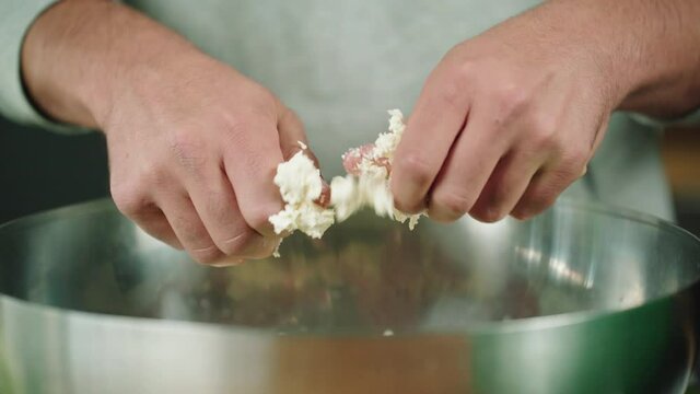 Hands crumbling feta cheese into a metal salad bowl.