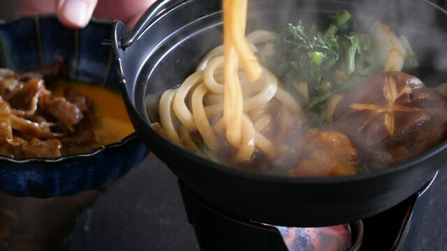 すき焼きのクローズアップ。煮込んでるうどんを生卵に付けて食べる動画。