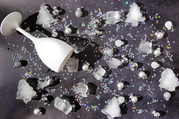 A white wine or Champagne glass on dark grey background with silver and white Christmas  balls, ice cubes and shiny silver tinsels in the shape of stars. Romantic creative concept for New Year card