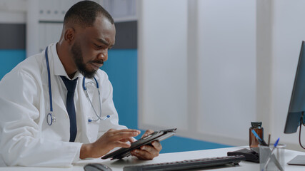African american therapist doctor holding tablet computer checking sickness report typing medical expertise. Physician man working at healthcare treatment in hospital office. Medicine concept