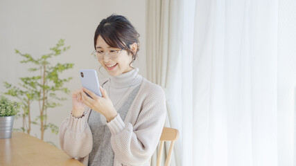 家でスマホを使う冬服のミドル女性