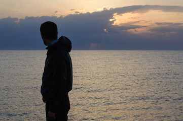 memories concept of silhouette of adult male in jacket with hood standing on sea shore looking at beautiful sky on ocean twilight dusk