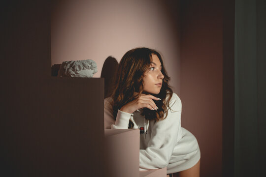 Young pretty woman in white sweater with curly hair opposite the lantern, on the pink background