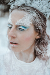 Stylized portrait of beautiful woman with art make up in snowy forest in winter. The Snow Queen concept.