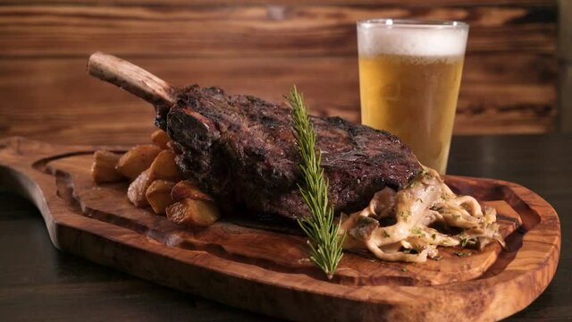 Mouthwatering bone in strip steak, roasted potatoes, wild woodear mushrooms and rosemary elegantly arranged on a wooden carving board with a frosty beer, slider HD