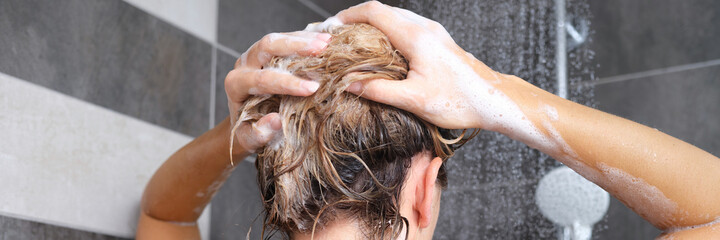Naklejka premium Woman washing her hair with shampoo in shower back view