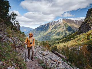 travel to Caucasus mountains in Karachay-Cherkessia, Arkhyz. Man in yellow hipster hoodie with photocamera hiking in mountains with travel backpack. Wandering lifestyle, adventure concept autumn