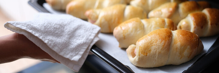 Housewife taking hot delicious mouth watering buns out of oven on baking sheet closeup