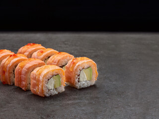 Japanese sake sushi roll with avocado and cream cheese inside roll. Asian dish pieces with burned salmon tataki on top on dark concrete background. Copy space image. Single object. Inside out sushi
