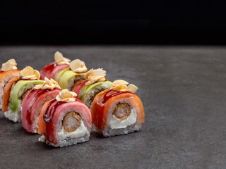 Crunchy black tiger shrimp inside Japanese sushi roll with cream cheese inside. Salmon, tuna, avocado slices on top served with sauce and peanut chips. Inside out sushi. Concrete background.

