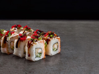 Crunchy black tiger shrimp inside Japanese sushi roll with cucumber inside. Salmon, eel, rockfish on top. red flying fish roe Tobiko. Masago caviar Asian roll. Inside out sushi. Concrete background.
