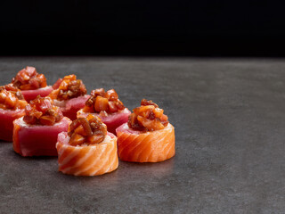 Japanese sushi roll with salmon and tuna. Asian dish pieces with marinated salmon on top on dark concrete background. Copy space image. Single object. Inside out sushi
