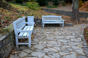 wooden bench on stone gray pavement in the park with low retaining walls stacked of porphyry....