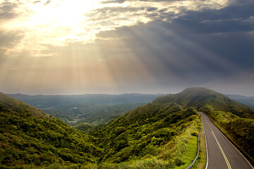 Beautiful sunset with sun rays over the contours of the mountains and a road along the top of the...