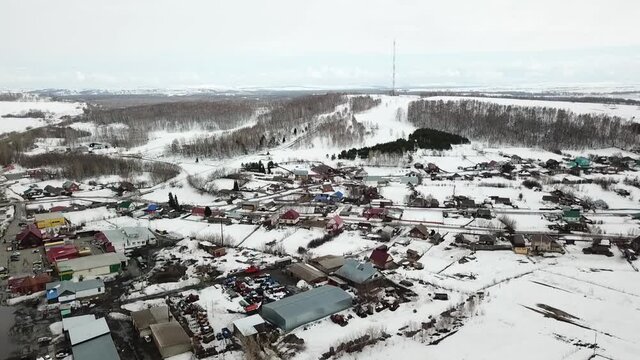 Slow take-off аerial shot of snowed deciduous forested hill with village under it when winter or early spring. Look like it's cell tower on the hill