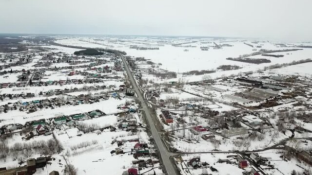 Aerial shot in movement of snowed village with intercity highway and distant fields. Winter or early spring