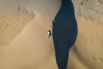 Woman lie on wavy sand dunes in desert landscape at sunset light.