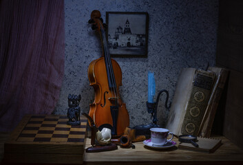 Retro still life with an old violin, smoking pipes, a chessboard and an elephant figure, two old books and a candle and a coffee cup