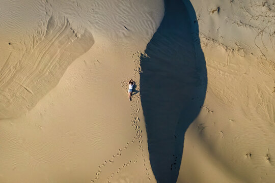 Woman lie on wavy sand dunes in desert landscape at sunset light.