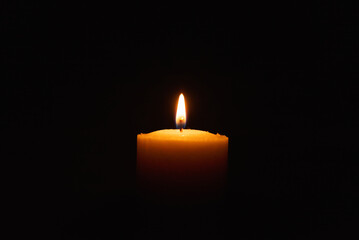 One single light candle burning brightly in the black background.Spiritual candle yellow flame. Flame of candle in the darkness.Copy space.