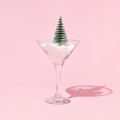Christmas tree and snow in martini cocktail glass on pastel pink background. Winter creative idea....