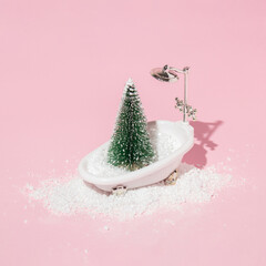 Christmas tree and snow in bath tub on pastel pink background. Winter creative idea. Retro...